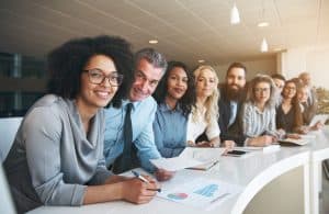 Portrait of a smiling group of diverse corporate colleagues standing in a row together at a table in a bright modern office