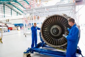 Engineers in uniforms assembling the turbine engine of a passenger jet at a hangar.