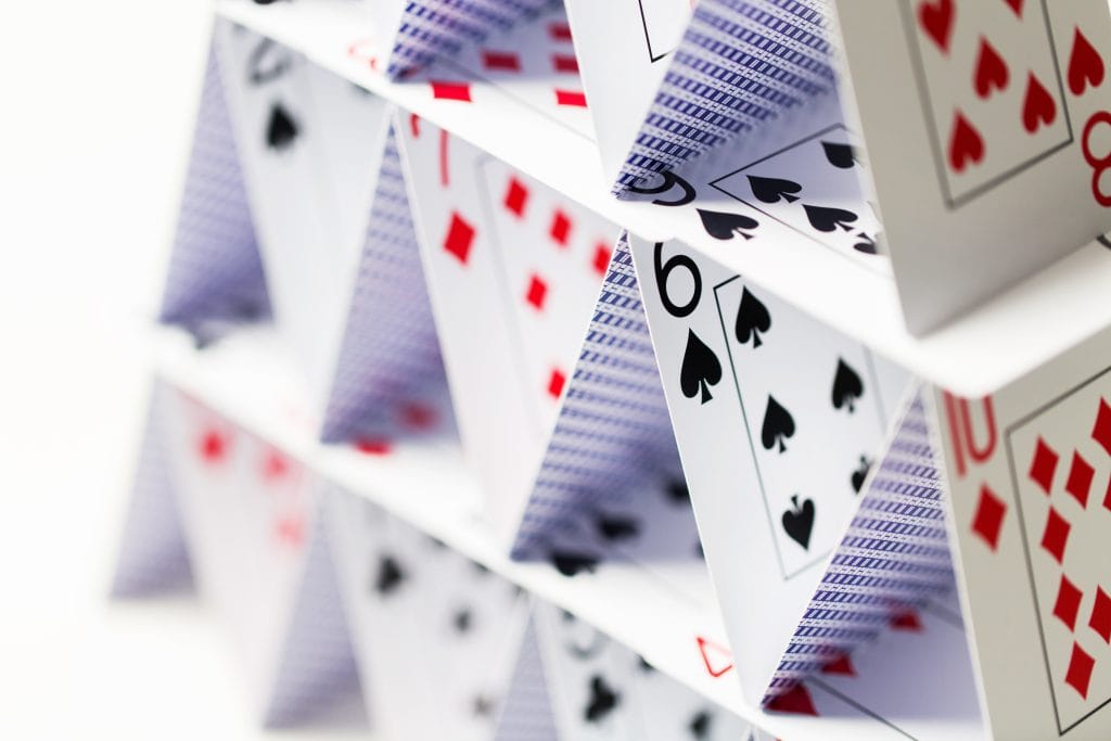 casino, gambling, games of chance, hazard and insecurity concept - close up of house of playing cards over white background