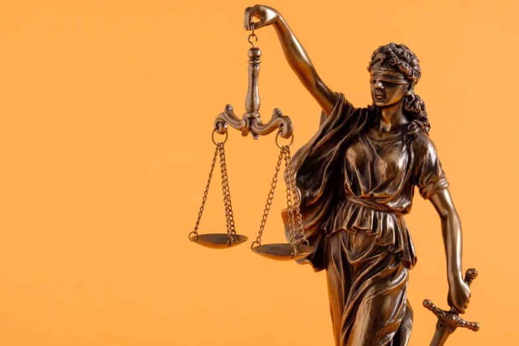 Brass figure of justice holding scales over a bright orange background with copy space