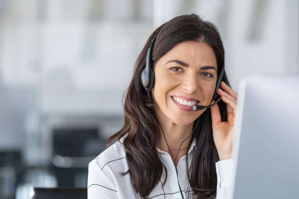 Call center agent with headset working on support hotline in modern office with copy space. Portrait of mature positive agent in conversation with customer over headset looking at camera.