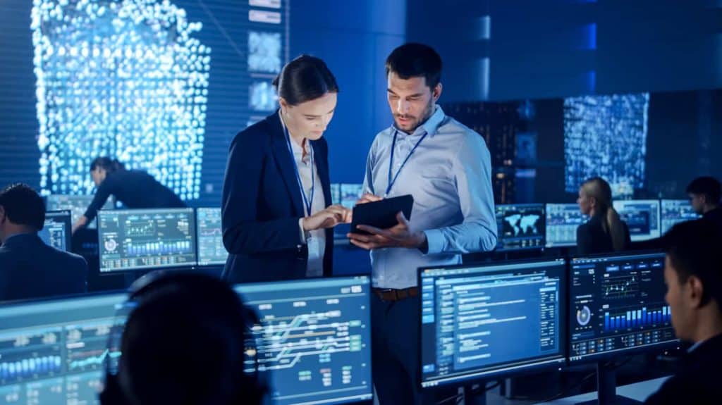 Project Manager and Computer Science Engineer Talking while Using A Digital Tablet Computer. Telecommunications Company System Control and Monitoring Office Room with Working Specialists.