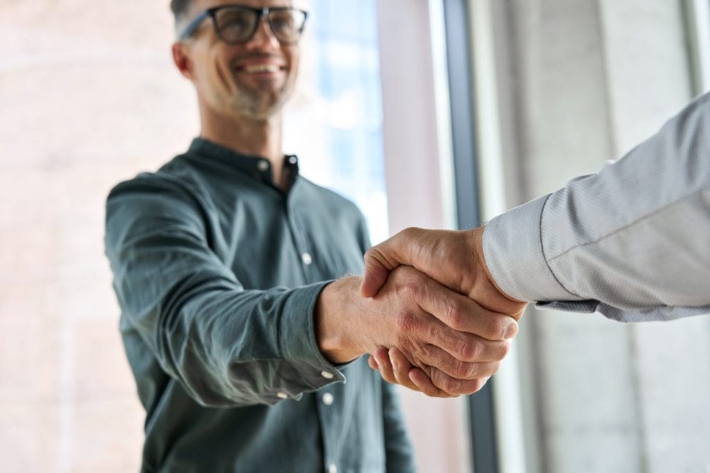 Two happy diverse professional business men executive leaders shaking hands at office meeting. Smiling businessman standing greeting partner with handshake. Leadership, trust, partnership concept.